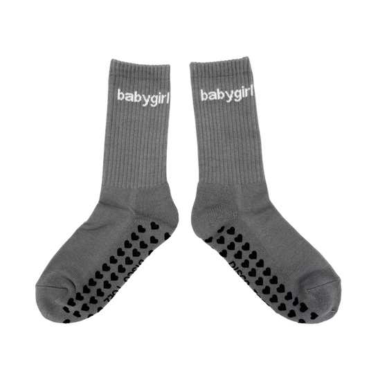 A pair of gray socks with the text 'babygirl' written on them. The socks have a textured sole designed for grip.